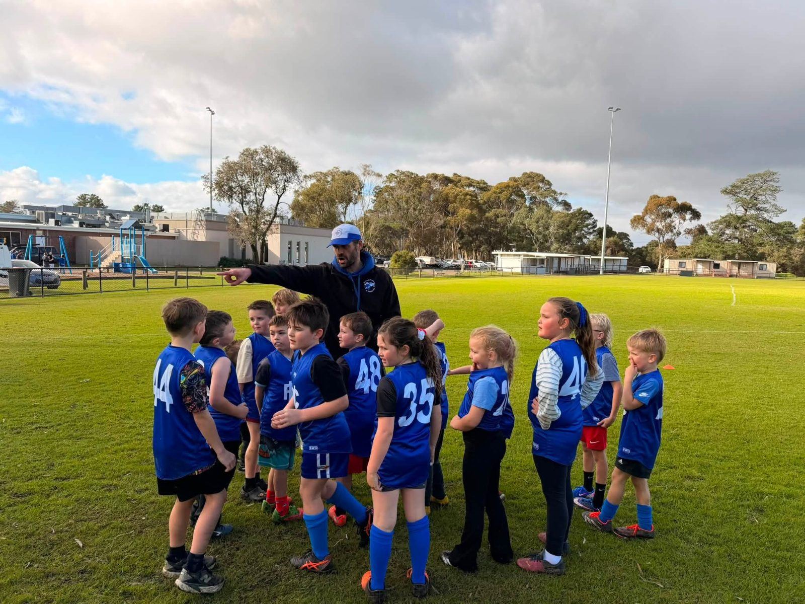 Young Auskickers gather around a coach on the oval at Hastings Park.