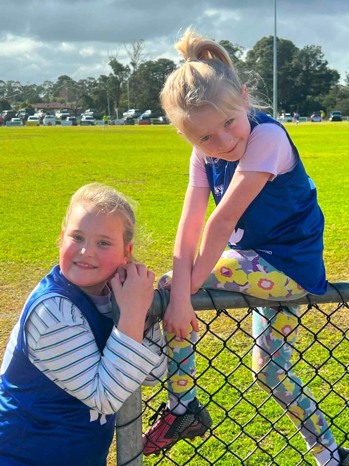 Two young Hastings players grin while climbing the fence beside the oval.