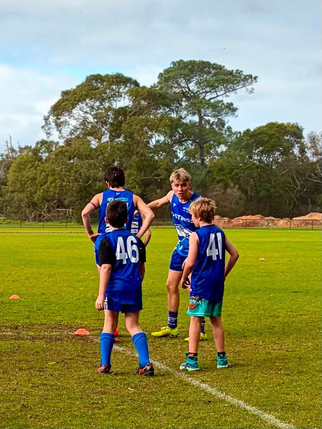Young players in Hastings colours stand on the oval, waiting for the next drill.