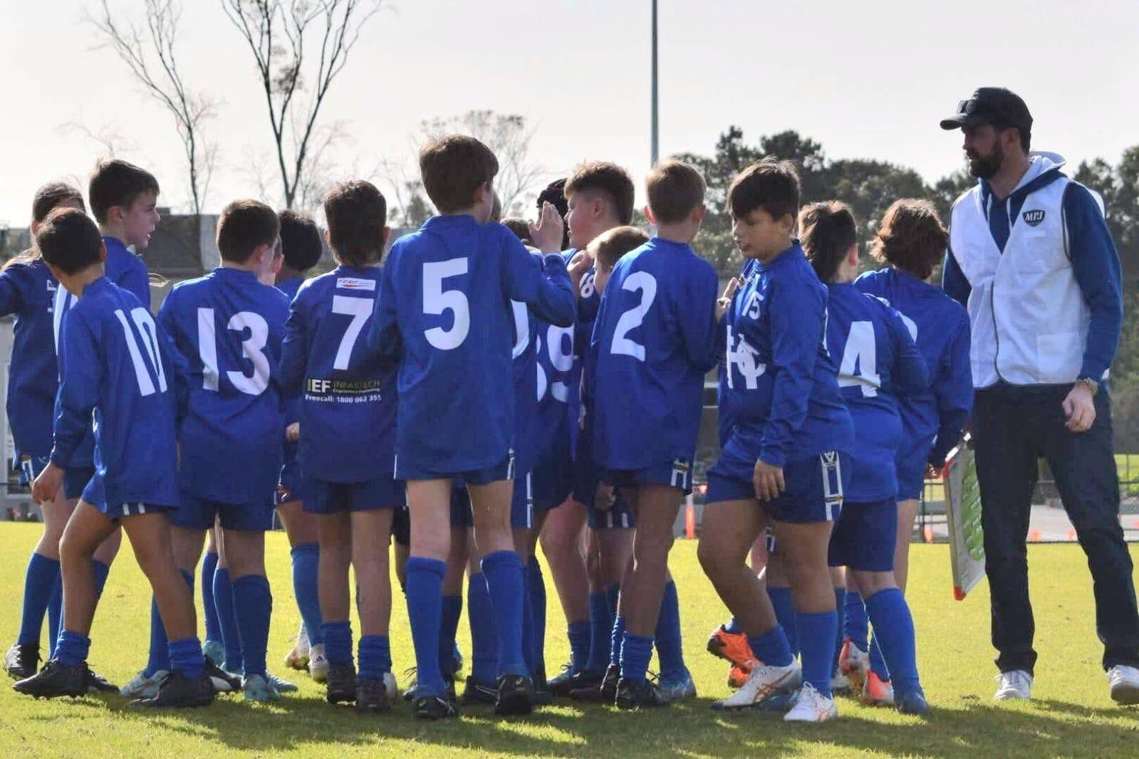 An older Hastings junior team huddles together with their coach before a game.